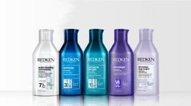 A row of 8 different colored bottles of Redken shampoos for all hair types against a white background.