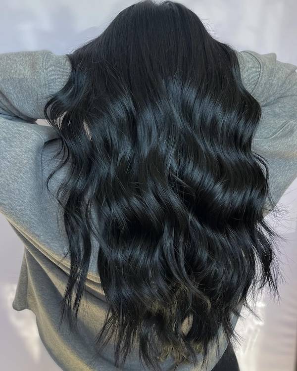 Long, glossy black hair styled in loose, flowing waves with a natural, healthy shine. The hair cascades down the back, creating a soft and elegant look.