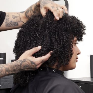 Image shows a woman with curly hair getting her hair styled by a Redken hairstylist