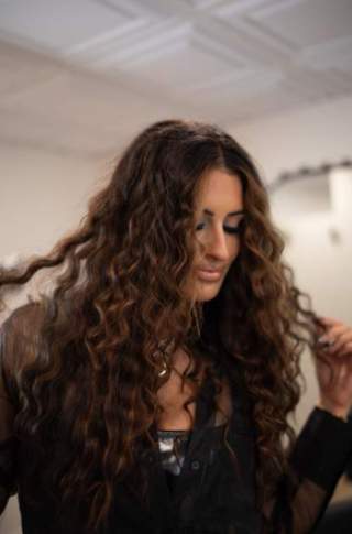 Woman with long, curly brunette hair holding the ends of her hair.