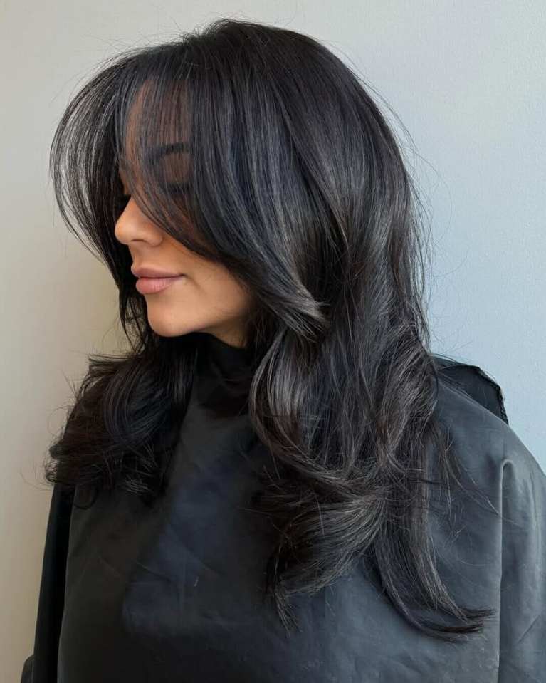 Side profile of a woman with long, dark hair styled with face-framing layers and soft waves after blowing out.