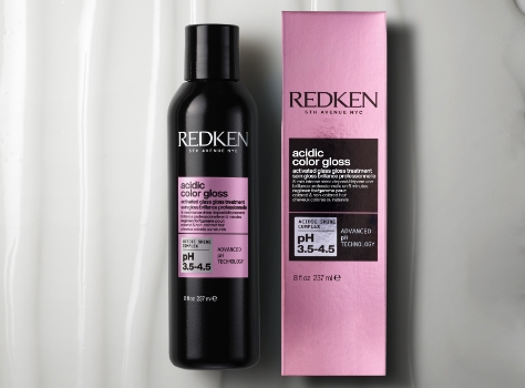 A bottle of Redken Acidic Color Gloss with a pink cap and a silver label with black text. The bottle is sitting in front of a white background.