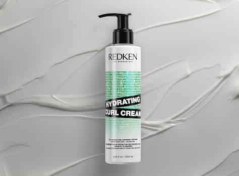 A bottle of Redken Acidic Bonding Concentrate Silicone-Free Conditioner surrounded by white liquid.
