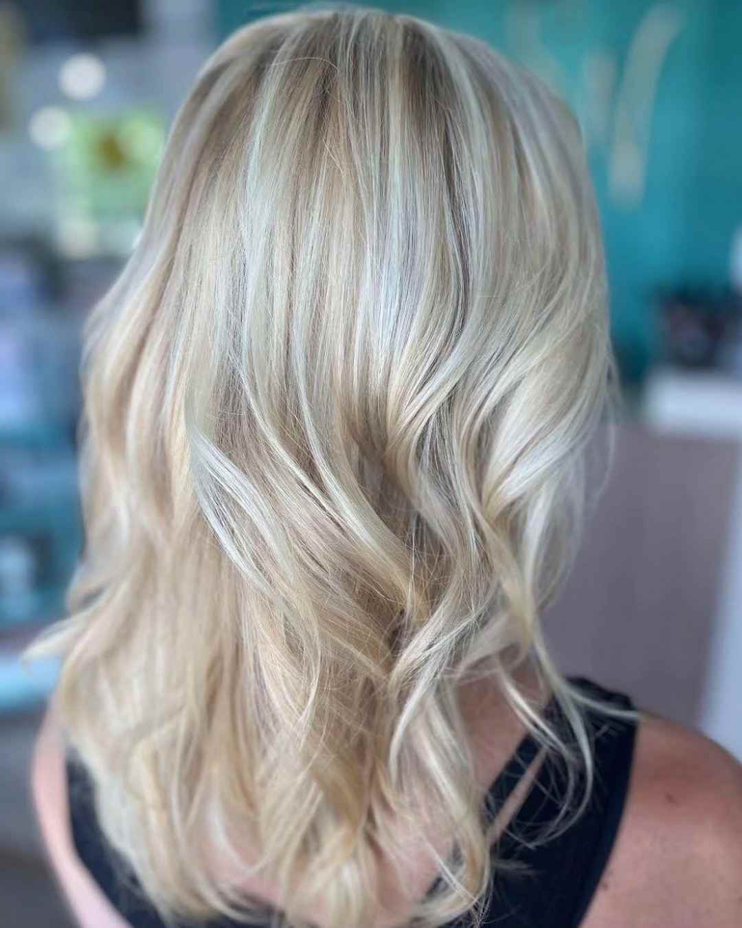  A back view of a person's medium-length, wavy blonde hair with highlights, showcasing healthy texture
