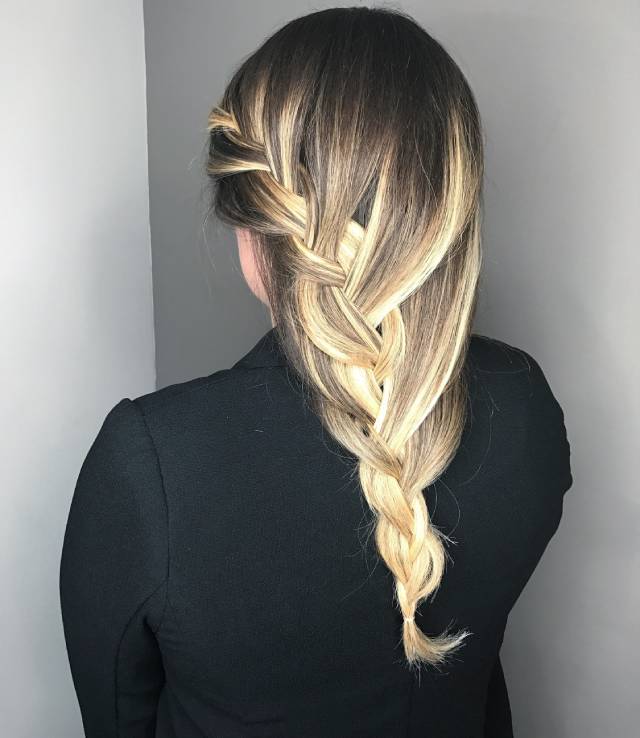 Blonde hair styled in a sleek, intricate fishtail braid that runs down the back. The braid highlights the hair’s natural tones and creates a polished yet playful look.