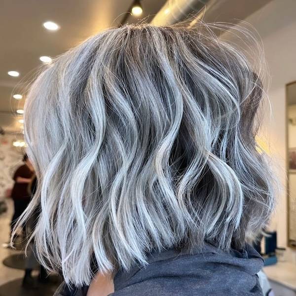 Medium-length silver hair styled in textured waves, showcasing a cool-toned, dimensional color. The waves add movement and volume, creating a chic and modern hairstyle